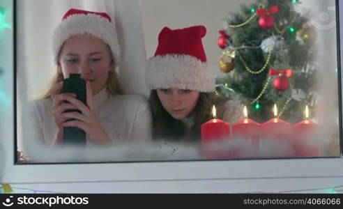 Little girls with gifted new smart phones at home near Christmas tree