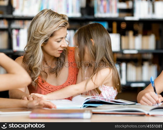 Little girls with their mother reading books in library. We love reading