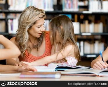 Little girls with their mother reading books in library. We love reading