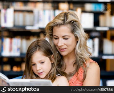 Little girls with their mother reading books in library. We love reading