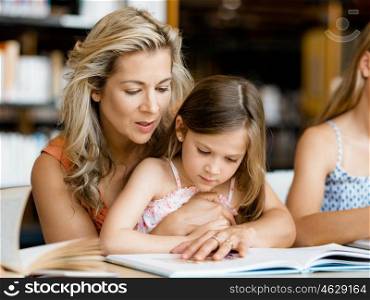 Little girls with their mother reading books in library. We love reading