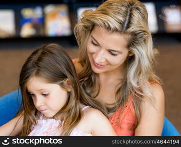 Little girls with their mother reading books in library. We love reading