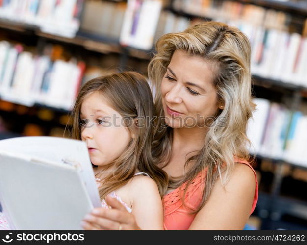 Little girls with their mother reading books in library. We love reading