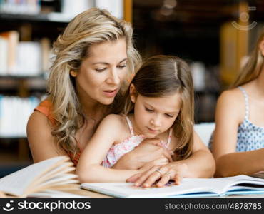 Little girls with their mother reading books in library. We love reading