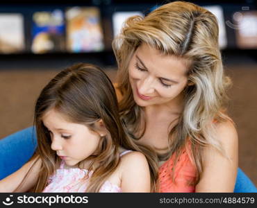 Little girls with their mother reading books in library. We love reading