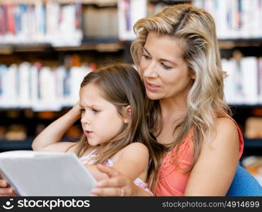 Little girls with their mother reading books in library. We love reading