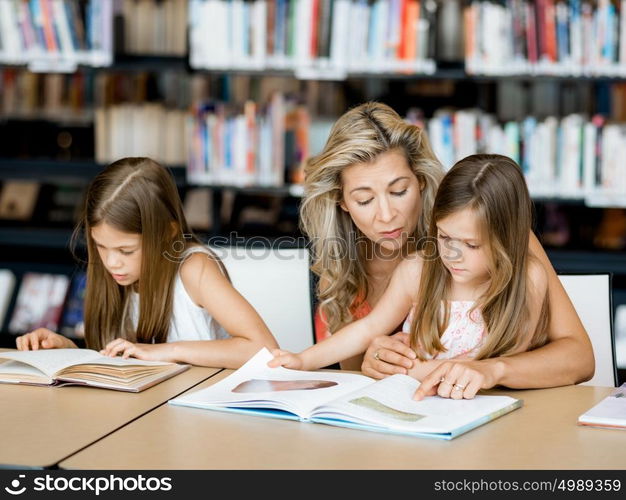 Little girls with their mother reading books in library. We love reading