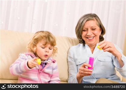 Little granddaughter with grandmother make bubble blower play happy together