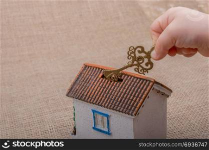 Little hand holding a retro key by a model house on a brown color background