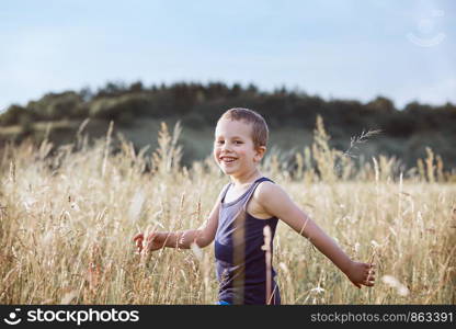 Little happy boy walking through a tall grass in the countryside. Candid people, real moments, authentic situations