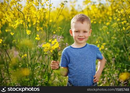 Little happy boy with a bouquet of flowers is in the yellow flowering rapeseed field