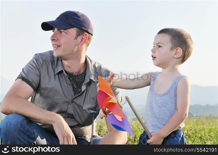 little happy child and young father play with windmil toy and have fun while running on beautiful meadow at sunset