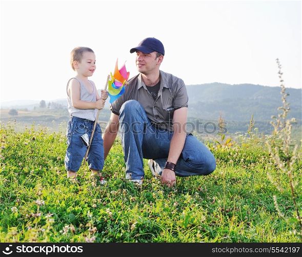 little happy child and young father play with windmil toy and have fun while running on beautiful meadow at sunset