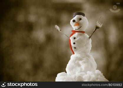 Little happy christmas snowman in blue screw top as hat red scarf with fork teaspoon outdoor. Winter season seasonal specific. Blurred background. Sepia tone.