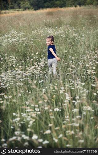 Little happy girl playing in a tall grass in the countryside. Candid people, real moments, authentic situations