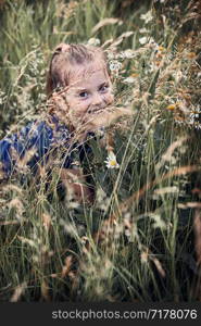 Little happy girl playing in a tall grass in the countryside. Candid people, real moments, authentic situations