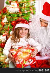 Little happy girl receive gift from Santa Claus, sitting near beautiful decorated Christmas tree, enjoying Xmas eve at home&#xA;