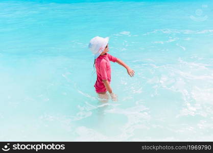 Little happy girl splashing in clear turquiose water. Cute little girl at beach during summer vacation