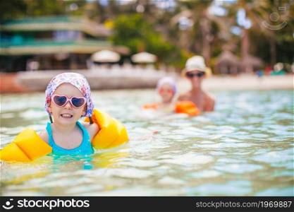Little happy girl splashing in clear turquiose water. Mother with little girl swim in the sea. Cute little girl at beach during summer vacation
