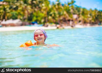 Little happy girl splashing in clear turquiose water. Cute little girl at beach during summer vacation