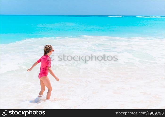 Little happy girl splashing in clear turquiose water in the sea. Cute little girl at beach during summer vacation