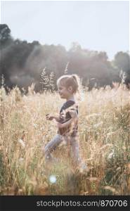 Little happy girl walking through a tall grass in the countryside. Candid people, real moments, authentic situations