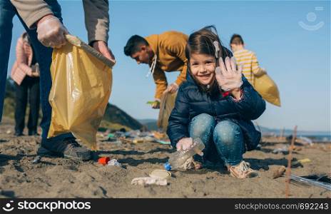 Little happy girl with volunteers picking up trash on the beach. Volunteers cleaning the beach