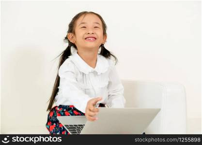 Little happy kid using laptop computer sitting on white sofa. Childhood lifestyle.