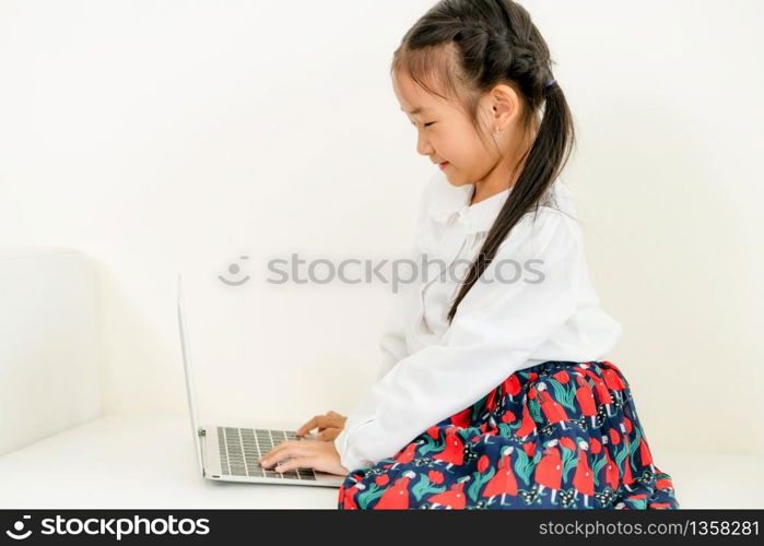 Little happy kid using laptop computer sitting on white sofa. Childhood lifestyle.