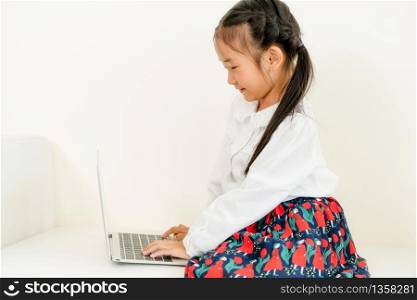 Little happy kid using laptop computer sitting on white sofa. Childhood lifestyle.