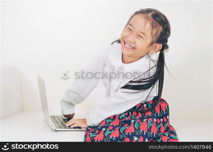 Little happy kid using laptop computer sitting on white sofa. Childhood lifestyle.. Little kid using laptop computer on white sofa.