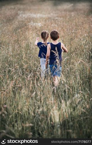 Little happy kids playing in a tall grass in the countryside. Candid people, real moments, authentic situations