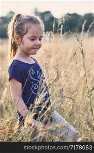 Little happy smiling girl playing in a tall grass in the countryside. Candid people, real moments, authentic situations
