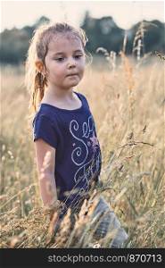Little happy smiling girl playing in a tall grass in the countryside. Candid people, real moments, authentic situations