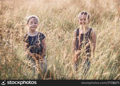 Little happy smiling kids playing in a tall grass in the countryside. Candid people, real moments, authentic situations