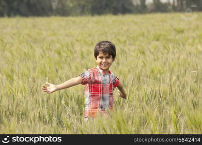 Little Indian boy standing in a wheat field with arms out