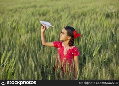 Little Indian girl holding a paper aero plane standing in wheat field