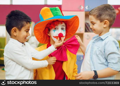 Little joyful boy touches red clown&rsquo;s nose, children playing together. Birthday party in playroom, baby holiday in playground. Childhood happiness, childish leisure. Little joyful boy touches red clown&rsquo;s nose