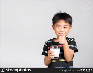 Little kid boy 5-6 years old smile holding milk glass he drinking white milk and show thumb up finger for good sign in studio shot isolated on white background, Daily life health care Medicine food