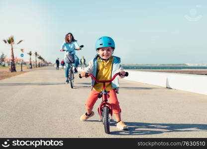 Little kid riding a balance bike with his mother on a bicycle in a city park