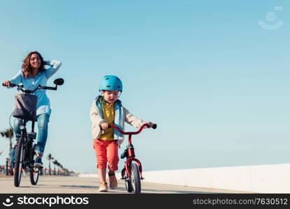 Little kid riding a balance bike with his mother on a bicycle in a city park