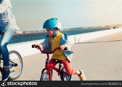 Little kid riding a balance bike with his mother on a bicycle in a city park