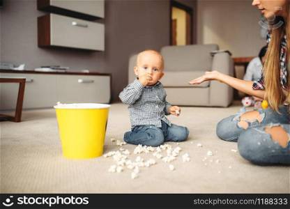 Little kid spilled popcorn on the floor, motherhood problems. Sad mom and son together at home, parenthood. Little kid spilled popcorn, motherhood problems