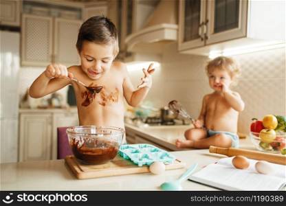 Little kids tastes melted chocolate. Cute boy and girl cooking on the kitchen. Happy children prepares sweet dessert at the table