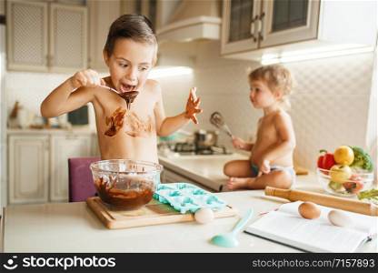 Little kids tastes melted chocolate. Cute boy and girl cooking on the kitchen. Happy children prepares sweet dessert at the table. Little kids tastes melted chocolate on the kitchen