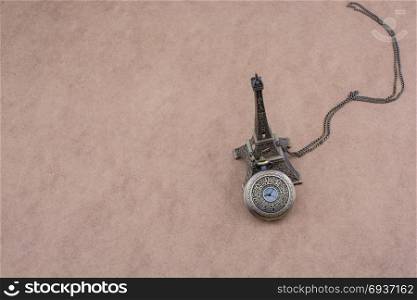 Little model Eiffel Tower and a pocket watch on brown background