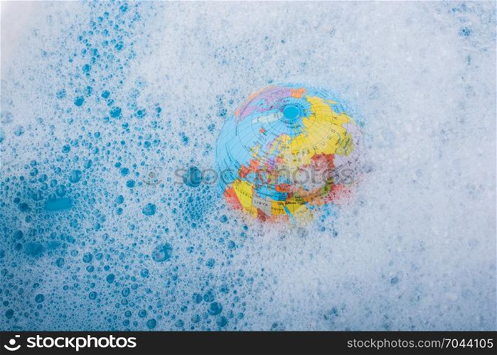 Little model globe floating in blue water covered with foam
