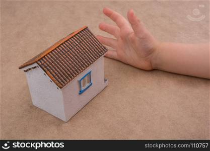 Little model house and a hand on a light brown color background