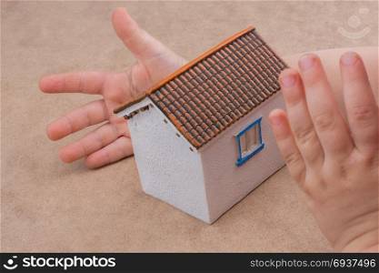 Little model house and a hand on a light brown color background