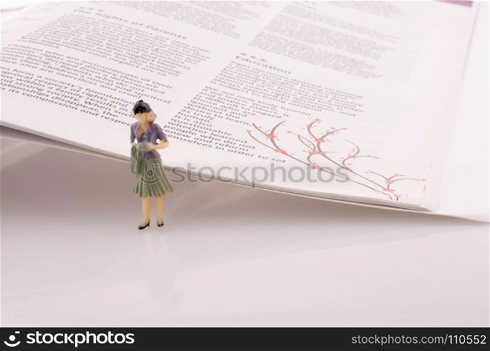 Little model woman figure standing by the side of the magazine pages
